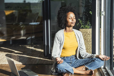 Young woman meditating in sunlight at home - UUF24686