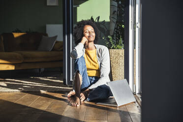 Woman with eyes closed relaxing in sunlight while sitting on floor at home - UUF24688