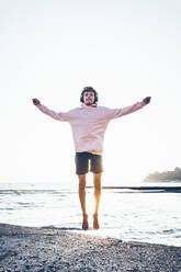 Carefree young man jumping at beach - OMIF00010