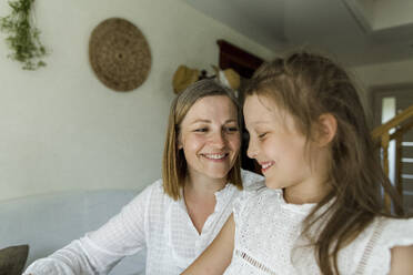 Lächelnde Frau sieht ihre Tochter im Wohnzimmer an - LLUF00034