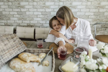 Lächelnde Tochter, die ihre Mutter umarmt, während sie am Esstisch isst - LLUF00039