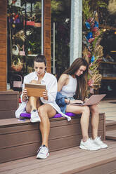 Freundinnen mit digitalem Tablet und Laptop auf einer Bank - OMIF00011