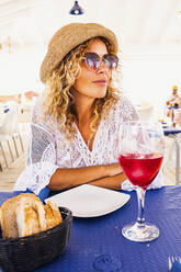 Frau mit Sonnenbrille sitzt mit Essen und Trinken am Tisch im Restaurant - SIPF02349