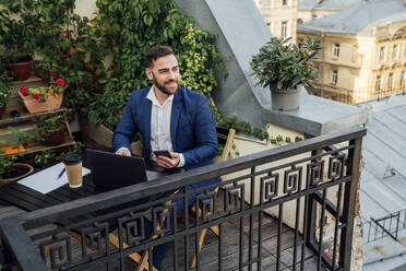 Männlicher Berufstätiger, der auf dem Balkon eines Büros sitzt und wegschaut - VPIF04728