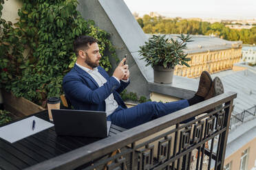 Businessman using smart phone while relaxing in office balcony - VPIF04735