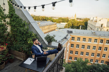 Männlicher Berufstätiger, der auf einem Balkon mit seinem Handy telefoniert - VPIF04736