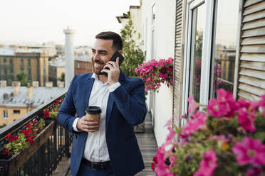 Männlicher Geschäftsmann, der auf dem Balkon eines Büros mit seinem Smartphone telefoniert - VPIF04746