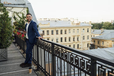 Männliche Fachkraft steht in der Nähe des Geländers auf dem Balkon eines Büros - VPIF04748