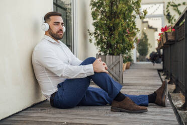 Geschäftsmann hört Musik beim Sitzen in der Nähe der Wand im Büro Balkon - VPIF04760