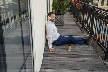 Male professional with reusable cup listening music in office balcony - VPIF04762