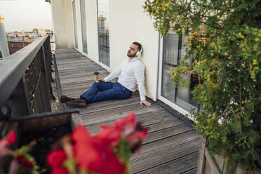 Male professional with disposable cup while listening music in balcony - VPIF04764