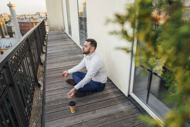 Männlicher Berufstätiger meditiert auf dem Balkon seines Büros - VPIF04765