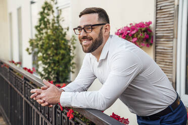 Lächelnder Geschäftsmann mit Brille lehnt am Geländer eines Bürobalkons - VPIF04768