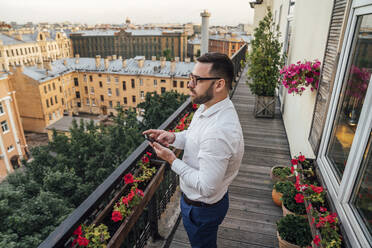 Male professional with smart phone standing in office balcony - VPIF04774