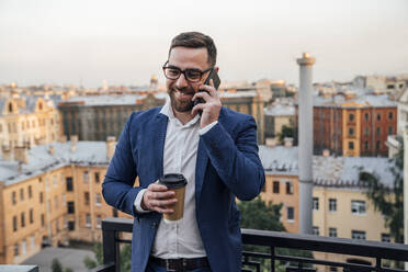 Male business person with disposable cup talking on smart phone in balcony - VPIF04781