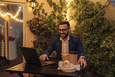 Männlicher Berufstätiger mit Laptop auf dem Balkon eines Büros bei Sonnenuntergang - VPIF04795