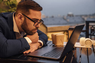 Businessman looking at laptop on table in office balcony - VPIF04802