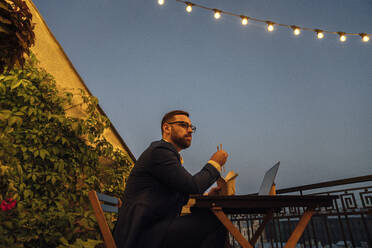 Businessman having food while sitting in office balcony - VPIF04808