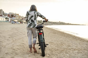 Älterer Mann fährt mit dem Fahrrad auf Sand am Strand - VEGF04959