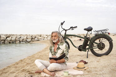 Mann schreibt in ein Buch, während er mit dem Fahrrad am Strand sitzt - VEGF04965