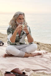 Man with mug sitting cross-legged at beach - VEGF04977