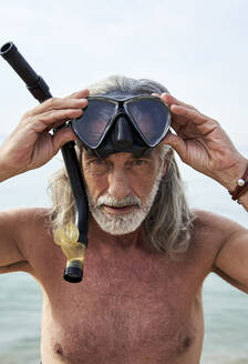Hemdenloser reifer Mann mit Schnorchelbrille am Strand - VEGF04984