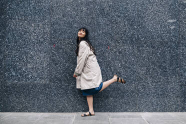 Frau steht auf einem Bein vor einer Wand - ASGF01471