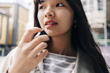 Young woman with long hair applying lip gloss - ASGF01476