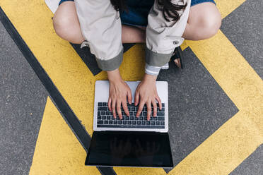 Junge Frau benutzt Laptop auf der Straße sitzend - ASGF01479