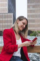 Weibliche Fachkraft, die auf einer Bank sitzend ein Mobiltelefon benutzt - PNAF02274