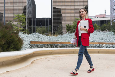 Businesswoman holding laptop while walking in city - PNAF02275