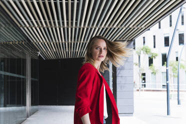 Weiblicher Berufstätiger mit rotem Blazer, der blonde Haare wirft - PNAF02286