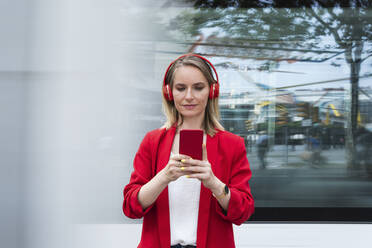 Geschäftsfrau mit drahtlosen Kopfhörern und Smartphone - PNAF02298
