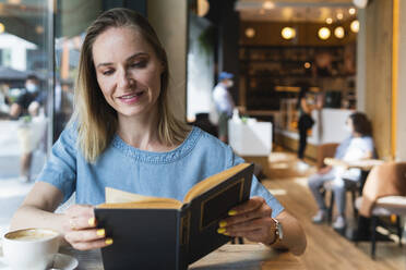 Blond businesswoman reading book at coffee shop - PNAF02302