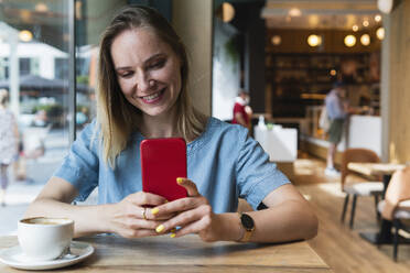 Freiberuflerin, die in einem Café sitzt und ihr Smartphone benutzt - PNAF02304