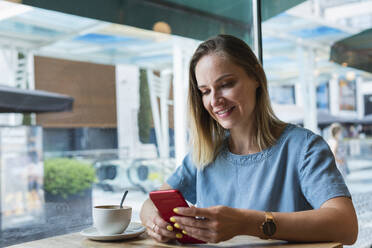 Female blond freelancer using mobile phone in coffee shop - PNAF02306