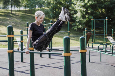 Frau balanciert mit hochgelegten Füßen auf einem Trainingsgerät im Park - LLUF00045