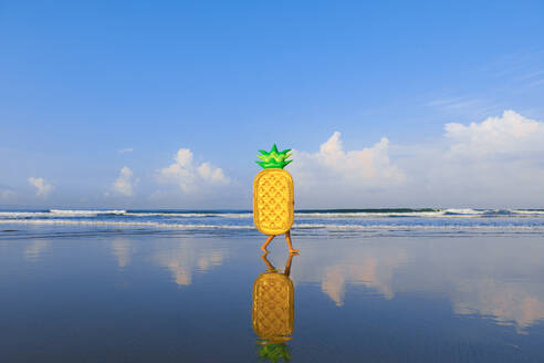 Woman with pineapple float walking at beach - EAF00114