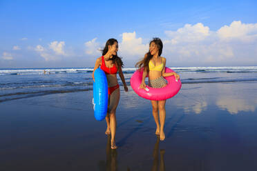 Fröhliche Freundinnen mit aufblasbaren Ringen haben Spaß am Strand - EAF00119