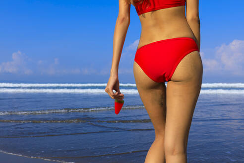 Woman in bikini holding ice cream at beach on sunny day - EAF00128