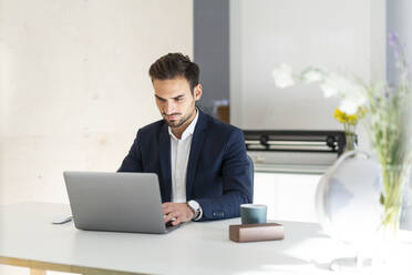 Junger Geschäftsmann, der einen Laptop benutzt, während er am Schreibtisch im Büro sitzt - MOEF03887