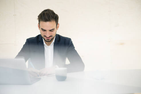 Junger männlicher Berufstätiger, der am Schreibtisch im Büro sitzt und schreibt - MOEF03908