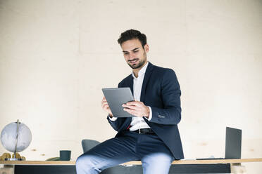Junge männliche Fachkraft, die ein digitales Tablet benutzt, während sie auf einem Schreibtisch im Büro sitzt - MOEF03913