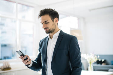 Gut aussehender junger Geschäftsmann, der im Büro stehend mit seinem Smartphone im Internet surft - MOEF03921