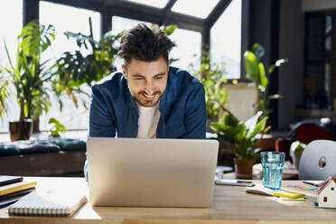 Smiling male professional using laptop while leaning on desk in office - BSZF01951