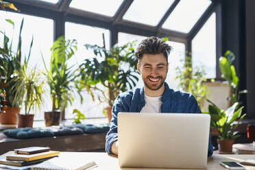 Happy male professional using laptop while sitting at desk in office - BSZF01954