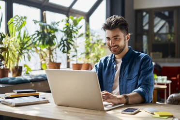 Lächelnde männliche Fachkraft arbeitet am Laptop am Schreibtisch im Büro - BSZF01956