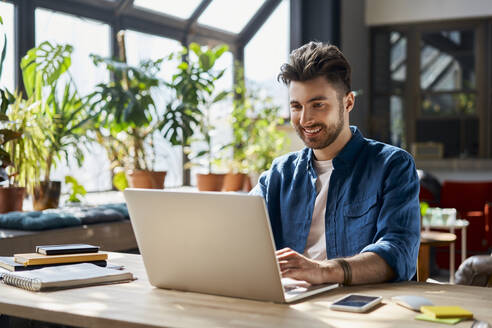 Smiling male professional working on laptop at desk in office - BSZF01956