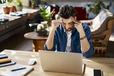 Tired businessman with head in hands sitting at desk in office - BSZF01958