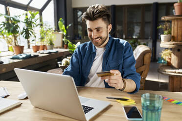 Männlicher Geschäftsmann mit Kreditkarte beim Online-Shopping im Büro - BSZF01960